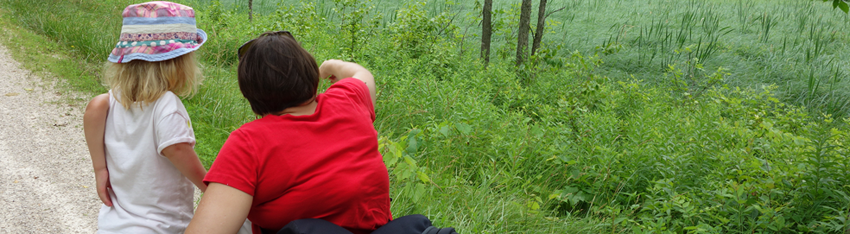 Photo of mother, a white woman and wheelchair user, and her daughter. They are looking out at a field and the mother is pointing ahead.